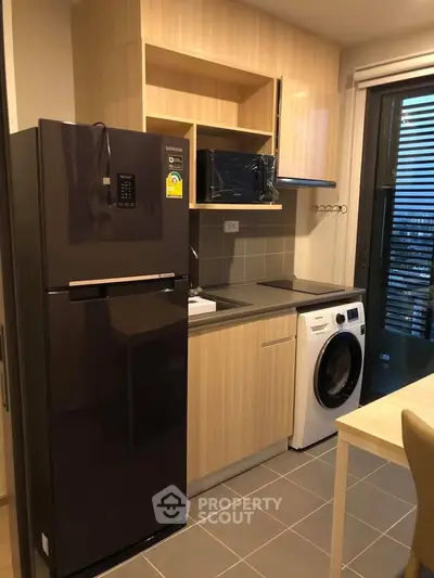 Modern kitchen with fridge, washing machine, and microwave in compact layout.