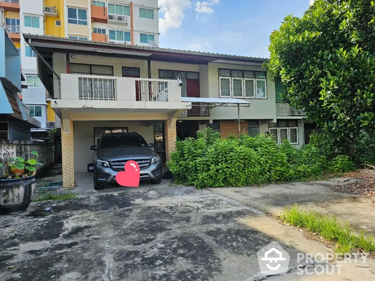 Charming two-story house with carport and lush greenery in urban setting.