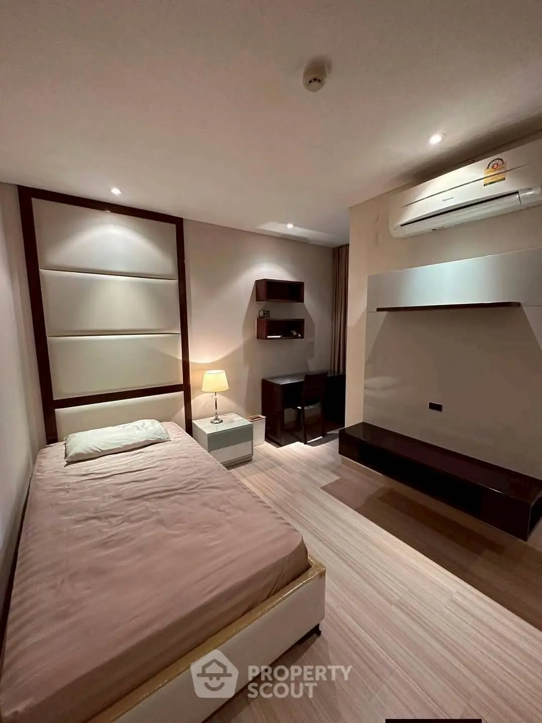 Modern bedroom with minimalist design, featuring a single bed, desk, and air conditioning unit.