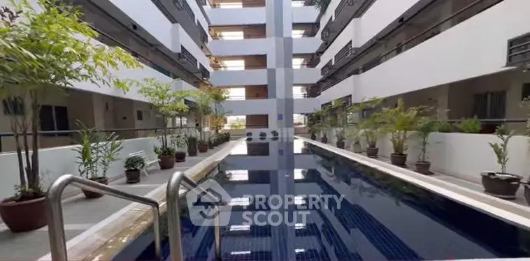 Modern apartment complex with sleek pool and lush greenery in shared courtyard.