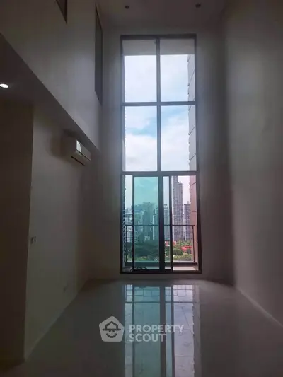 Spacious high-ceiling room with floor-to-ceiling windows and city view