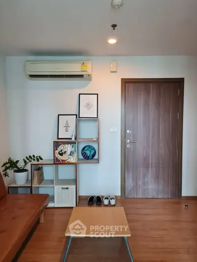 Modern living room with stylish decor and wooden flooring, featuring a cozy seating area and wall-mounted air conditioning.