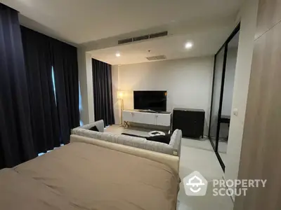 Modern bedroom with a large bed, sleek furniture, and a flat-screen TV, complemented by dark curtains and ambient lighting for a cozy atmosphere.