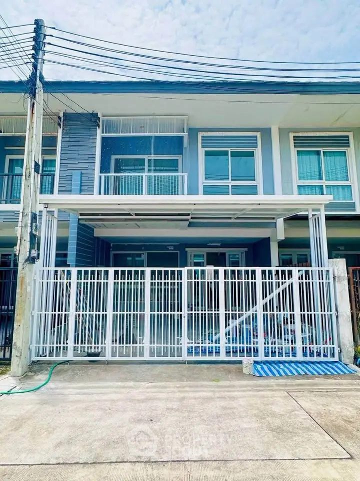 Modern two-story townhouse with gated entrance and large windows in a suburban neighborhood.