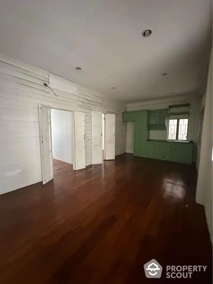 Spacious open-plan living area with wooden flooring and green kitchen cabinets.