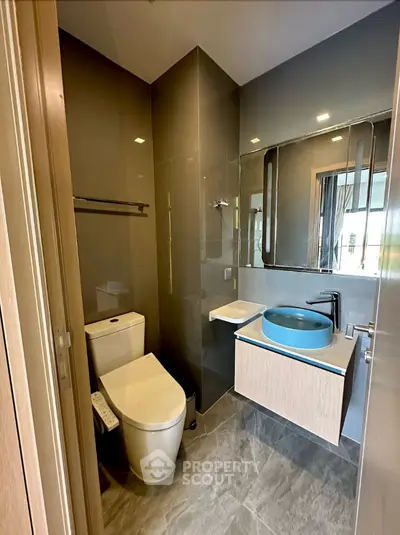 Modern bathroom with sleek design, featuring a unique blue basin, large mirror, and glass shower enclosure, perfect for contemporary living.