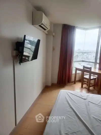 Cozy bedroom with wall-mounted TV and city view from large window.