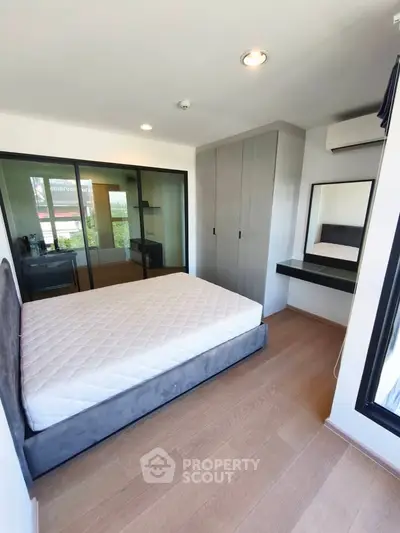 Modern bedroom with large window, built-in wardrobe, and sleek wooden flooring.