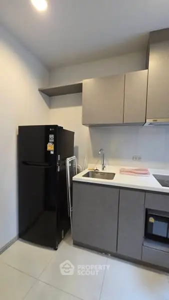 Modern kitchen with sleek cabinets and black refrigerator in compact layout.