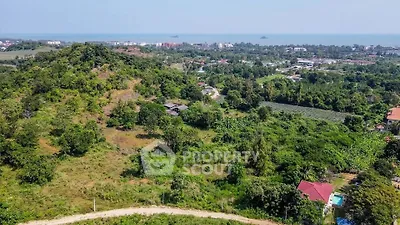 Expansive aerial view of a lush green plot of land with potential for development, surrounded by trees and with a distant ocean view, ideal for a luxury estate or resort.
