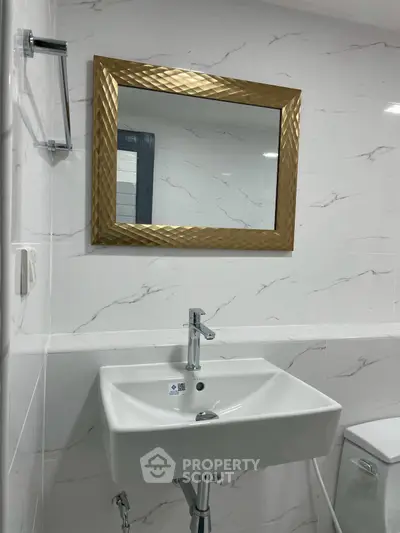 Modern bathroom with elegant gold-framed mirror and sleek white sink.