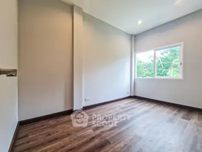 Spacious empty room with wooden flooring and large window overlooking greenery.