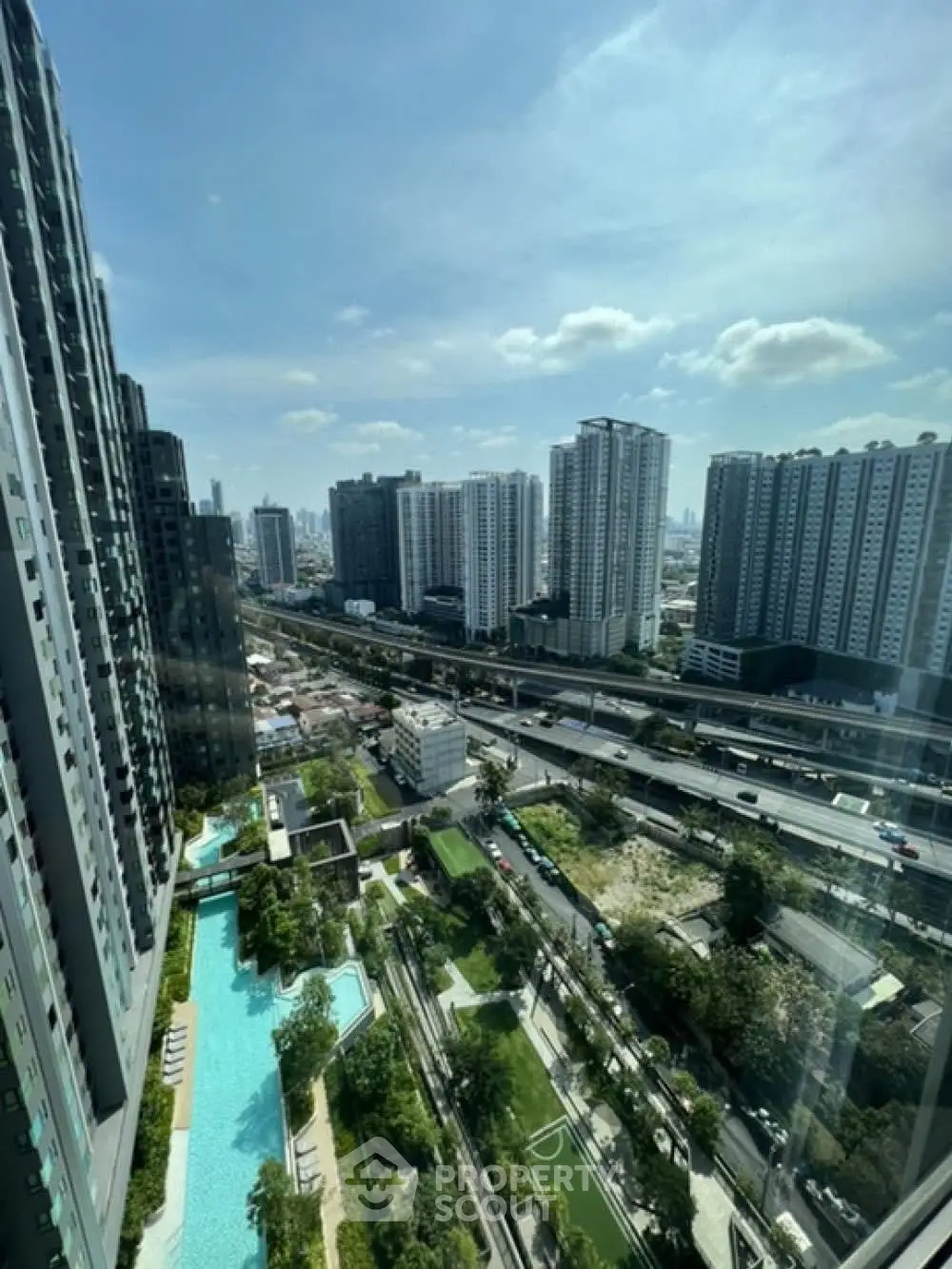 Stunning cityscape view from high-rise apartment with pool and lush greenery.