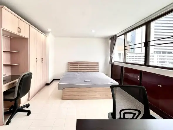 Spacious bedroom with modern furniture and large windows offering city views.