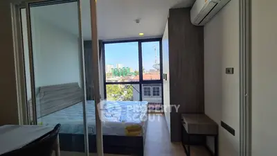 Modern bedroom with large window offering city view, featuring sleek furniture and air conditioning.