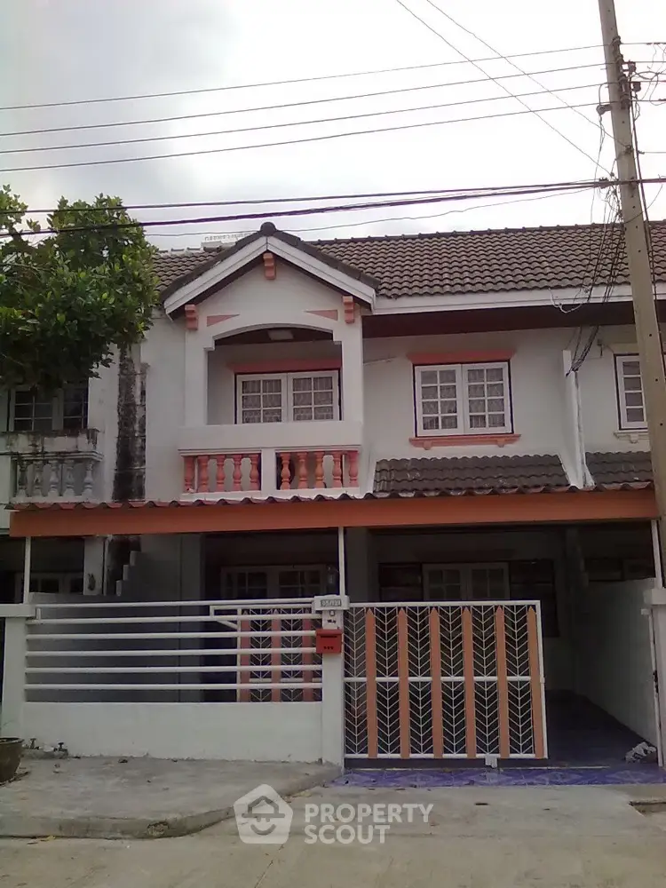 Charming two-story residential home with a classic tiled roof and a secure gated entrance, featuring a spacious carport and quaint upper-level balcony.