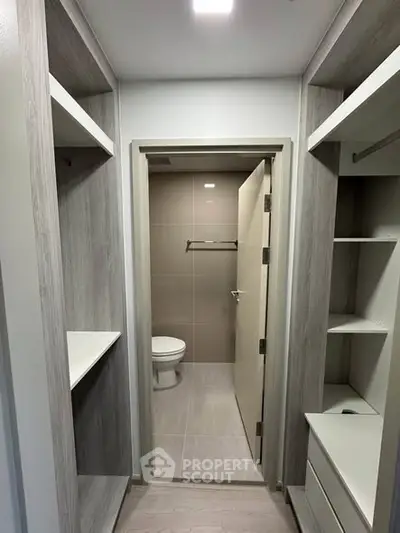 Modern walk-in closet leading to a sleek bathroom with neutral tones and ample storage space.