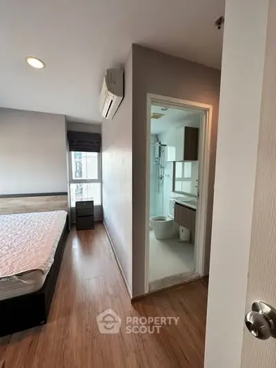 Modern bedroom with ensuite bathroom, featuring wooden flooring and natural light.