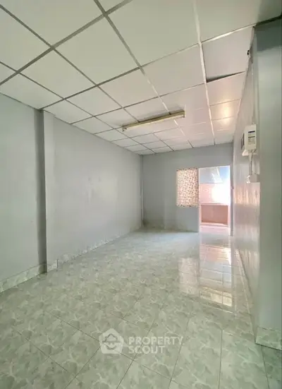 Spacious empty room with tiled flooring and window, ideal for customization.