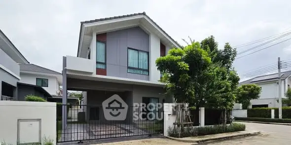 Modern two-story house with gated entrance and lush greenery in suburban neighborhood.