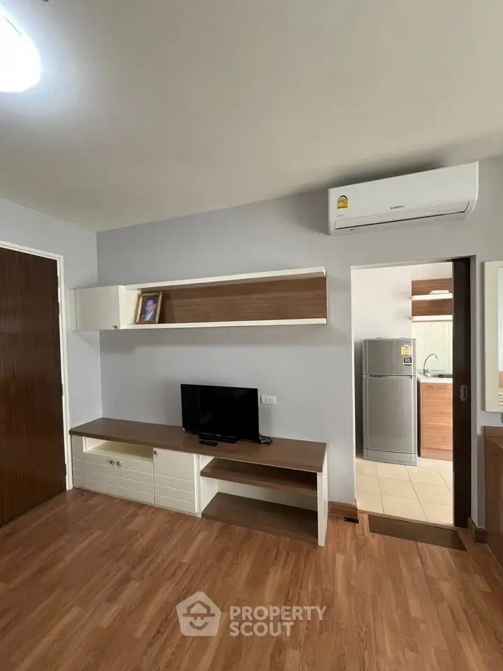 Modern living room with wooden flooring and built-in TV unit, adjacent to a sleek kitchen.