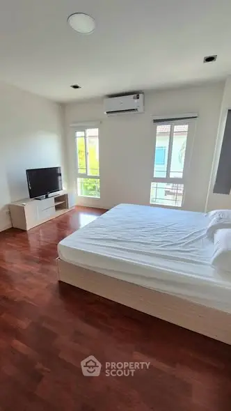 Spacious bedroom with hardwood floors, large windows, and modern furnishings.