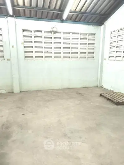 Spacious industrial-style room with concrete floor and large windows, ideal for storage or workshop use.