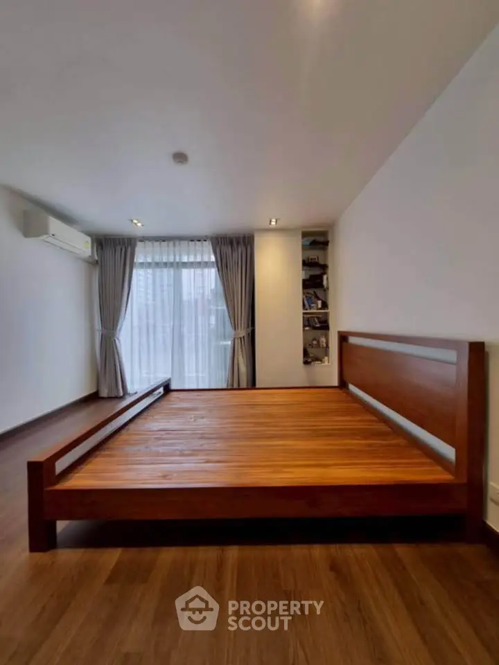 Spacious bedroom with wooden flooring and large window for natural light.