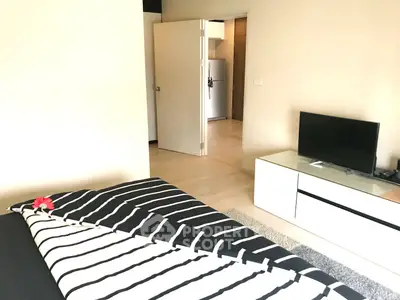 Modern bedroom with stylish decor and TV unit, leading to a kitchen area with a fridge.