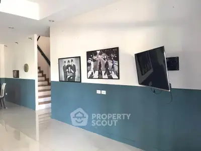 Modern living room with stylish decor and wall-mounted TV, featuring iconic artwork and sleek staircase.