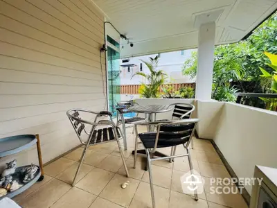 Spacious covered balcony with a metal table and chairs set, perfect for outdoor dining or relaxation, surrounded by lush greenery.