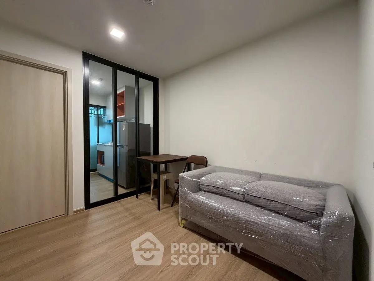 Modern apartment interior with compact living room and kitchen, featuring sleek glass partition and cozy furnishings.