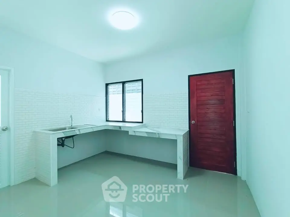 Spacious kitchen with modern white countertops and red door