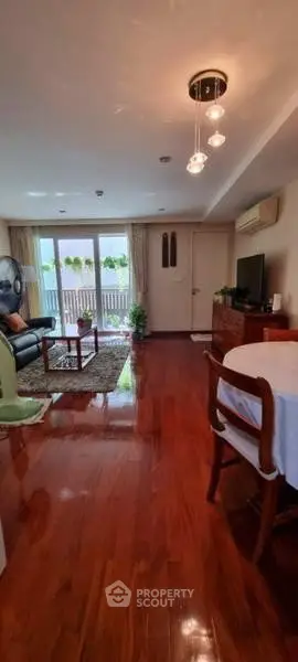 Spacious living room with wooden flooring and modern decor, featuring a cozy seating area and large windows.