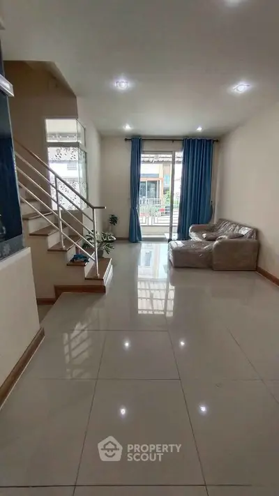 Spacious living room with modern staircase and large windows for natural light.