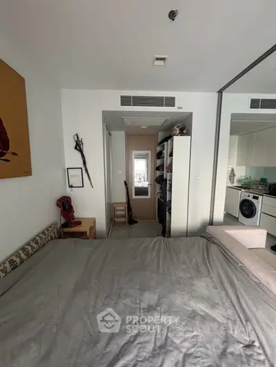 Cozy bedroom with modern decor and mirrored closet doors, adjacent to a compact kitchen.