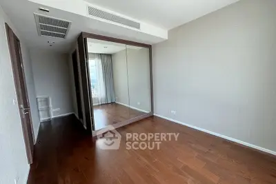 Spacious bedroom with wooden flooring and large mirrored closet in modern apartment.