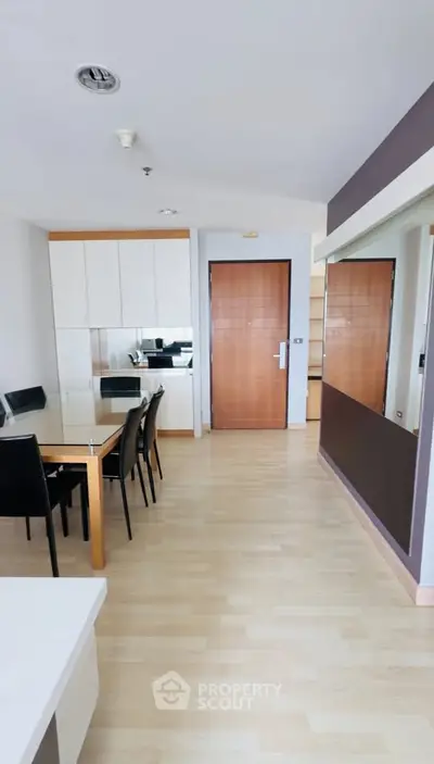 Modern apartment interior with dining area and kitchen, featuring sleek wooden flooring and contemporary furniture.