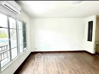 Spacious empty room with wooden flooring and large windows, perfect for customization.
