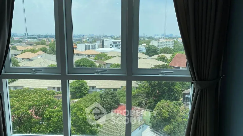 Stunning cityscape view from a high-rise window overlooking lush greenery and rooftops.