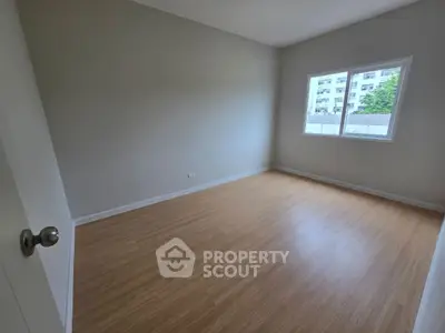 Spacious empty bedroom with wooden flooring and large window view.