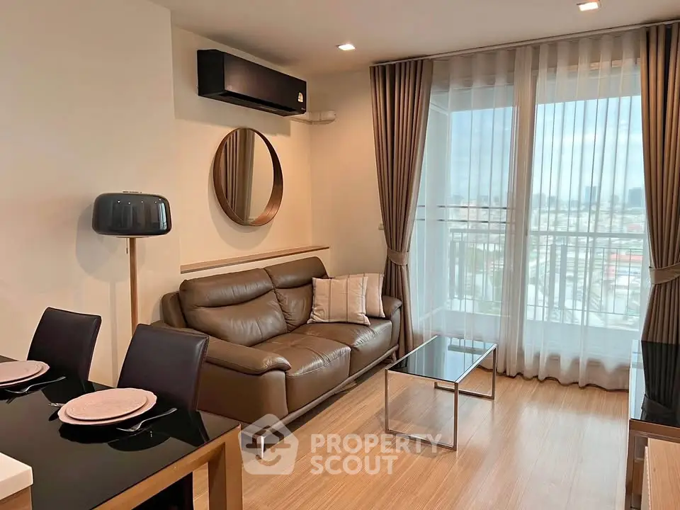 Modern living room with leather sofa, dining area, and city view from large window.