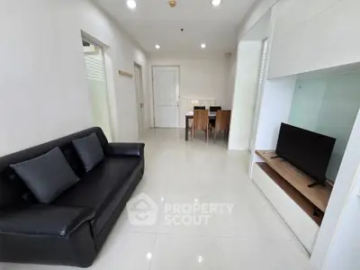 Modern living room with sleek black sofa and wall-mounted TV in a bright, minimalist apartment.