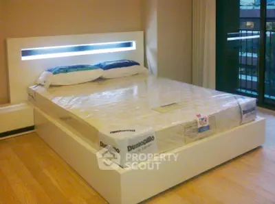 Modern bedroom with sleek bed frame and large window offering natural light.