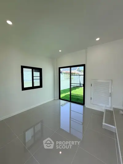 Spacious modern room with glossy tiled floor and large windows overlooking a green lawn.
