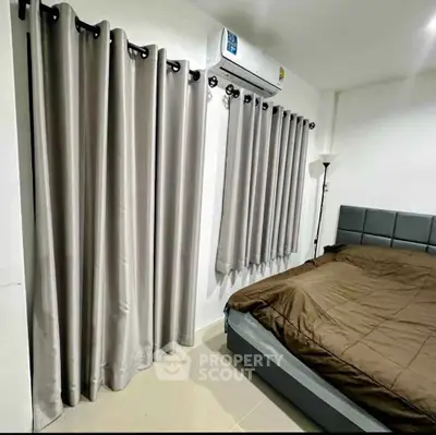 Modern bedroom with sleek curtains and air conditioning, featuring a cozy bed and minimalist decor.