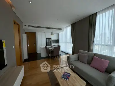 Modern living room with open kitchen, featuring sleek furniture and large windows with city view.