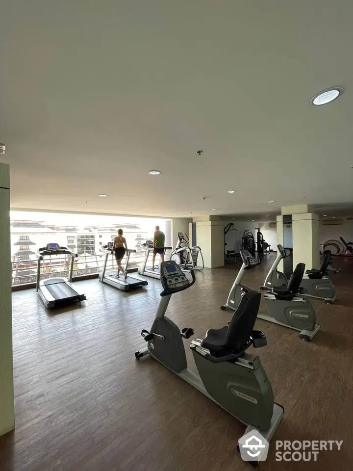 Spacious gym with modern equipment and city view in luxury apartment complex.