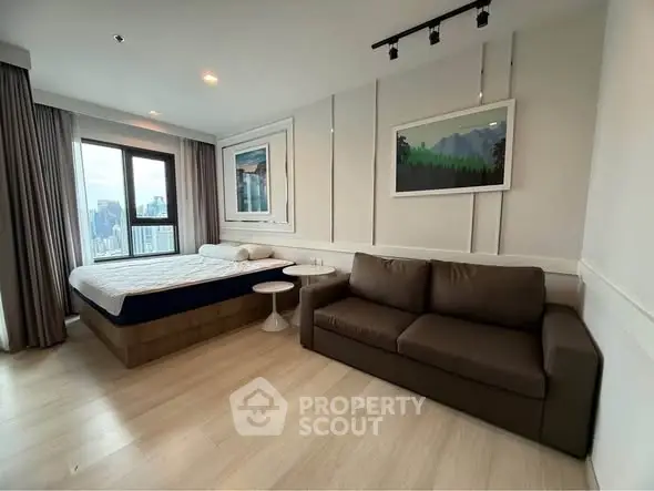 Modern bedroom with city view, featuring a cozy bed and stylish sofa in a bright, airy space.
