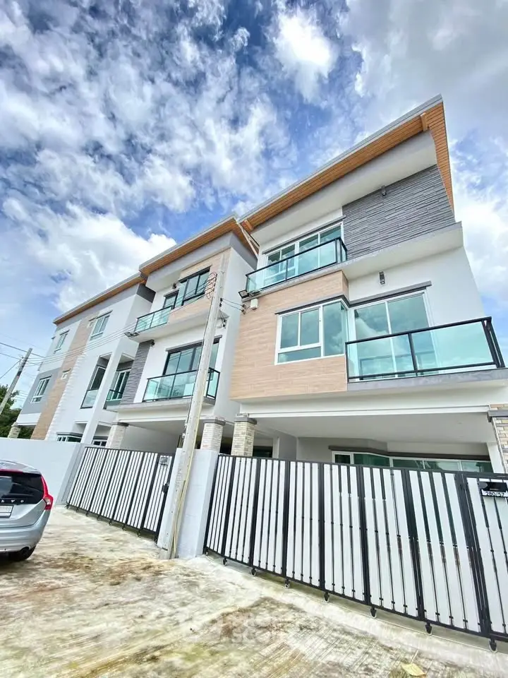 Modern multi-story townhouse with glass balconies and sleek design under a vibrant sky.